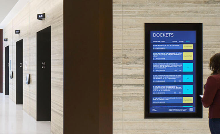 A digital docket display screen mounted in a courthouse hallway showing a real-time list of family law dockets.